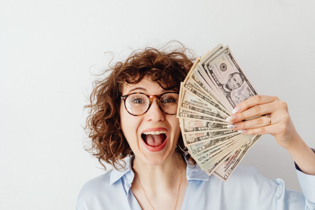 Smiling woman holding stack of cash because she is financially independent