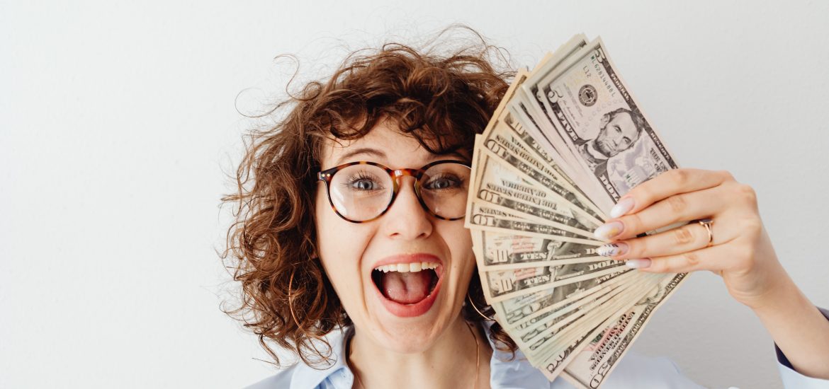 Smiling woman holding stack of cash because she is financially independent