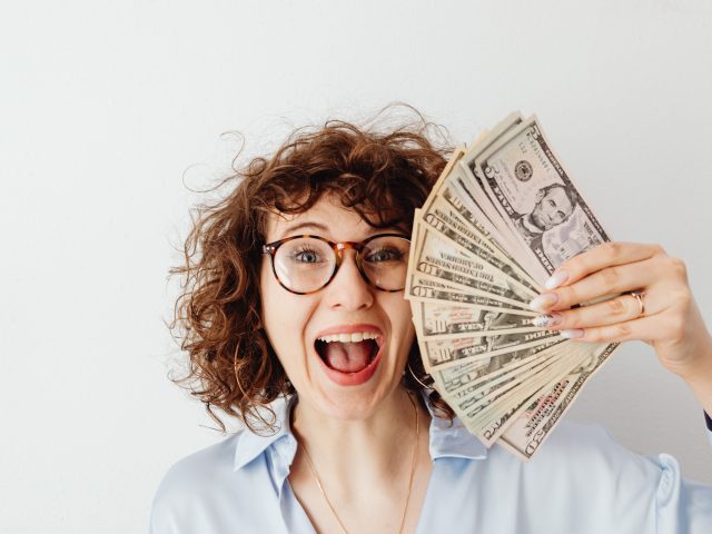 Smiling woman holding stack of cash because she is financially independent