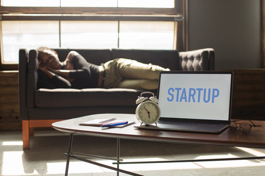 Individual napping on a couch behind an open laptop that reads "STARTUP"