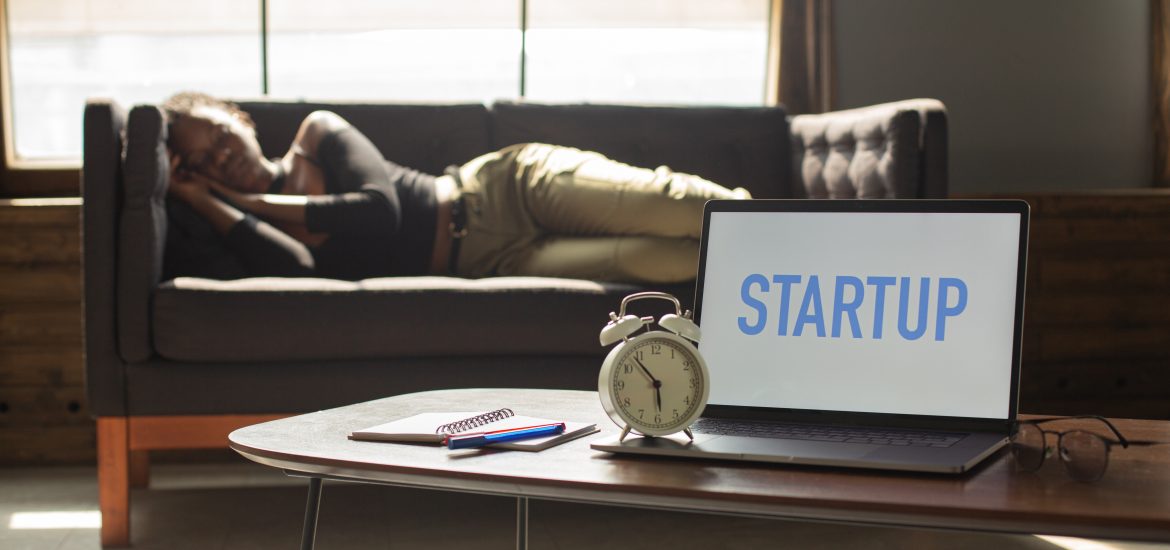 Individual napping on a couch behind an open laptop that reads "STARTUP"