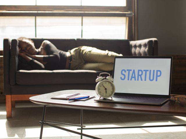 Individual napping on a couch behind an open laptop that reads "STARTUP"